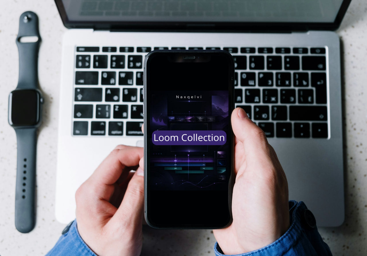 Person holding a smartphone with 'Loom Collection' app displayed, in front of a laptop and smartwatch on a desk.